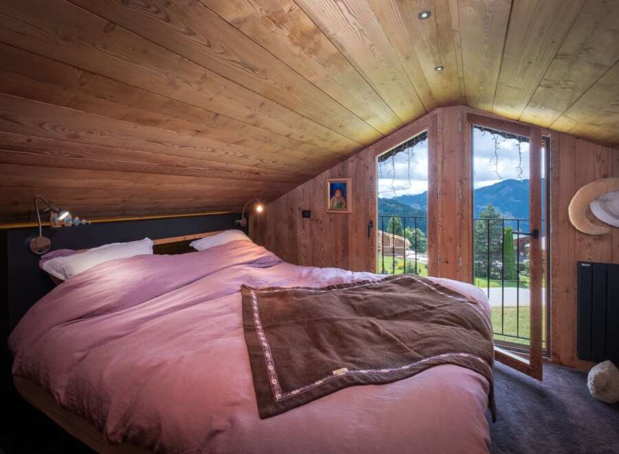 Experience the charm of this cozy bedroom, featuring a warm wooden interior and a stunning mountain view from the balcony.
