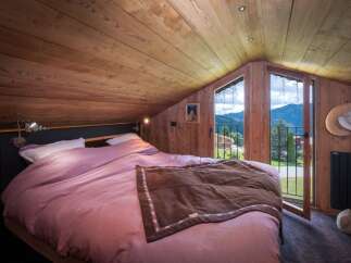 Experience the charm of this cozy bedroom, featuring a warm wooden interior and a stunning mountain view from the balcony.
