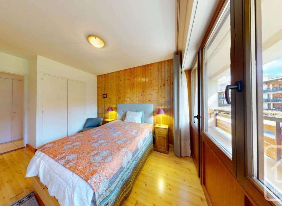 Discover this charming bedroom featuring a cozy bed with a vibrant patterned cover and a wooden accent wall.
