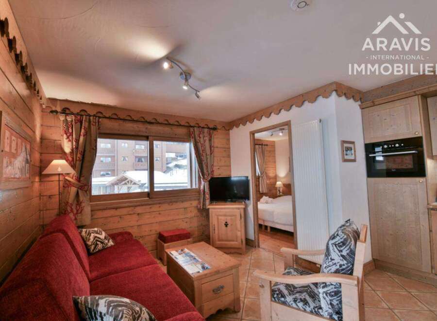 Discover the charm of this cozy apartment, featuring a warm wooden interior and a comfortable red sofa.