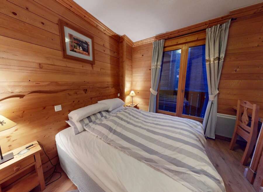 Step into this cozy bedroom featuring beautiful wood paneling and a comfortable bed with striped bedding.