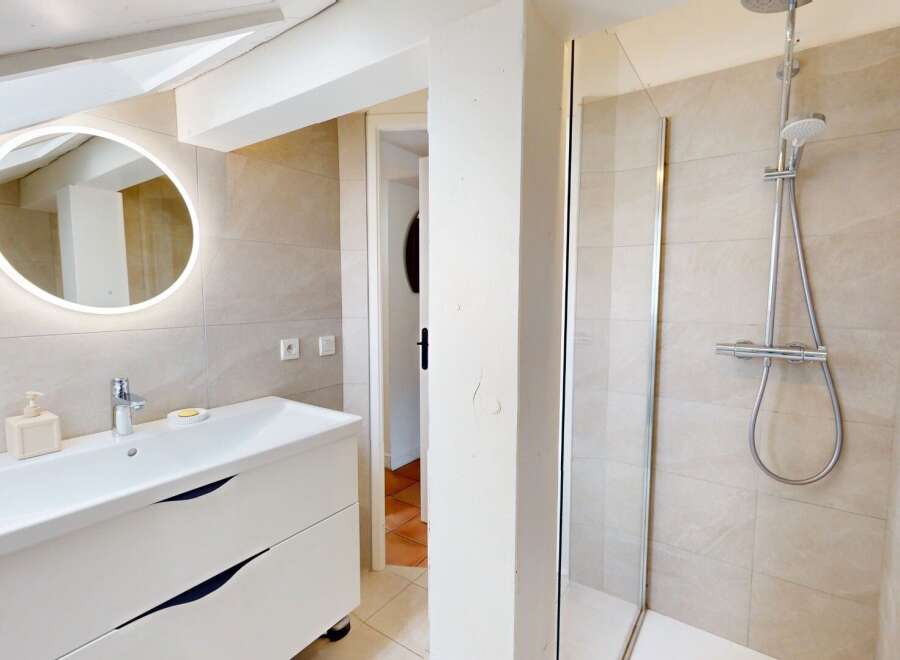 This modern bathroom features a sleek white vanity with ample storage and a stylish round mirror with integrated lighting.