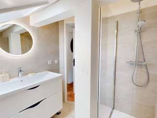 This modern bathroom features a sleek white vanity with ample storage and a stylish round mirror with integrated lighting.