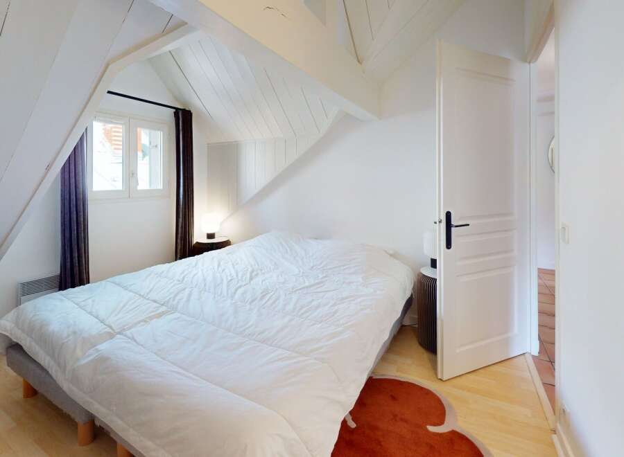 Discover the charm of this cozy bedroom, featuring a comfortable bed and a unique sloped ceiling design.