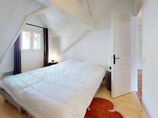 Discover the charm of this cozy bedroom, featuring a comfortable bed and a unique sloped ceiling design.