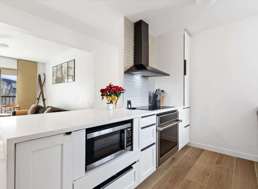 This modern kitchen boasts sleek white cabinetry, stainless steel appliances, and a stylish range hood.