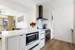 This modern kitchen boasts sleek white cabinetry, stainless steel appliances, and a stylish range hood.
