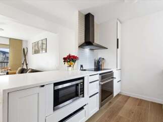 This modern kitchen boasts sleek white cabinetry, stainless steel appliances, and a stylish range hood.