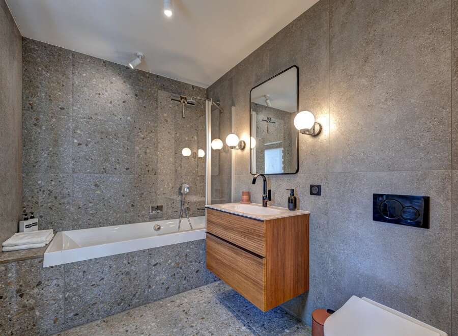 This modern bathroom boasts a sleek design with its gray tiled walls and flooring, creating a sophisticated and contemporary ambiance.