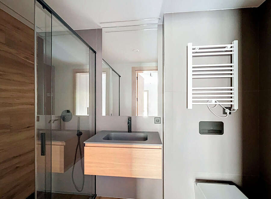 Step into a modern bathroom oasis! This stunning space features a sleek glass shower enclosure, a stylish floating vanity with a wooden cabinet, and a contemporary sink.