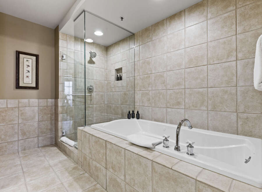 Indulge in the luxury of this spa-like bathroom, featuring a sleek glass-enclosed shower and a deep soaking tub.