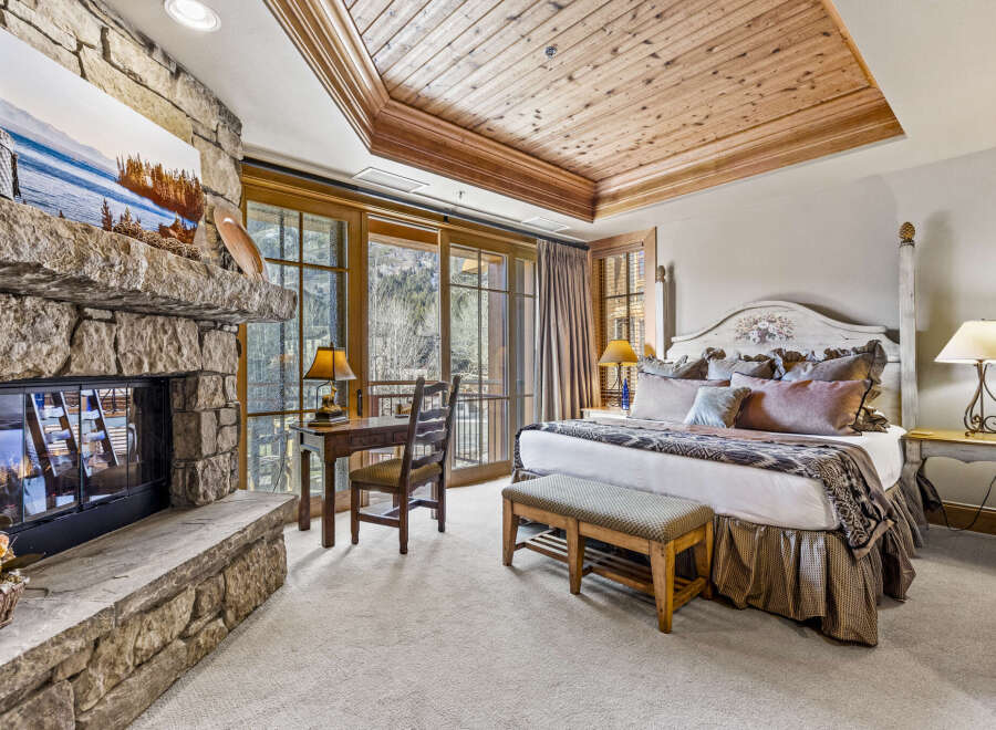 Experience luxury and comfort in this stunning bedroom featuring a cozy fireplace and a beautiful wooden ceiling.