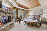 Experience luxury and comfort in this stunning bedroom featuring a cozy fireplace and a beautiful wooden ceiling.