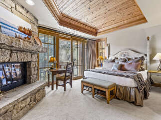 Experience luxury and comfort in this stunning bedroom featuring a cozy fireplace and a beautiful wooden ceiling.