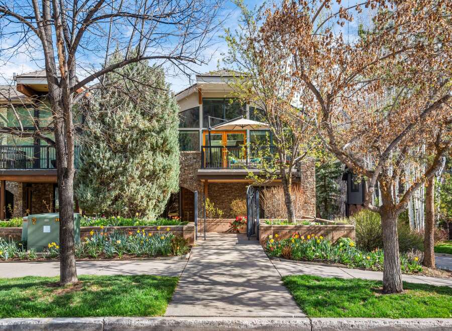 Charming townhouse featuring a multi-level stone and wood facade, complemented by lush landscaping and vibrant spring tulips.