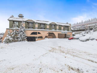 Nestled in a winter wonderland, this property showcases a charming exterior with snow-covered roofs and lush evergreen trees.