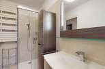 This modern bathroom features a sleek shower with glass doors, a stylish vanity, and a tall storage cabinet.