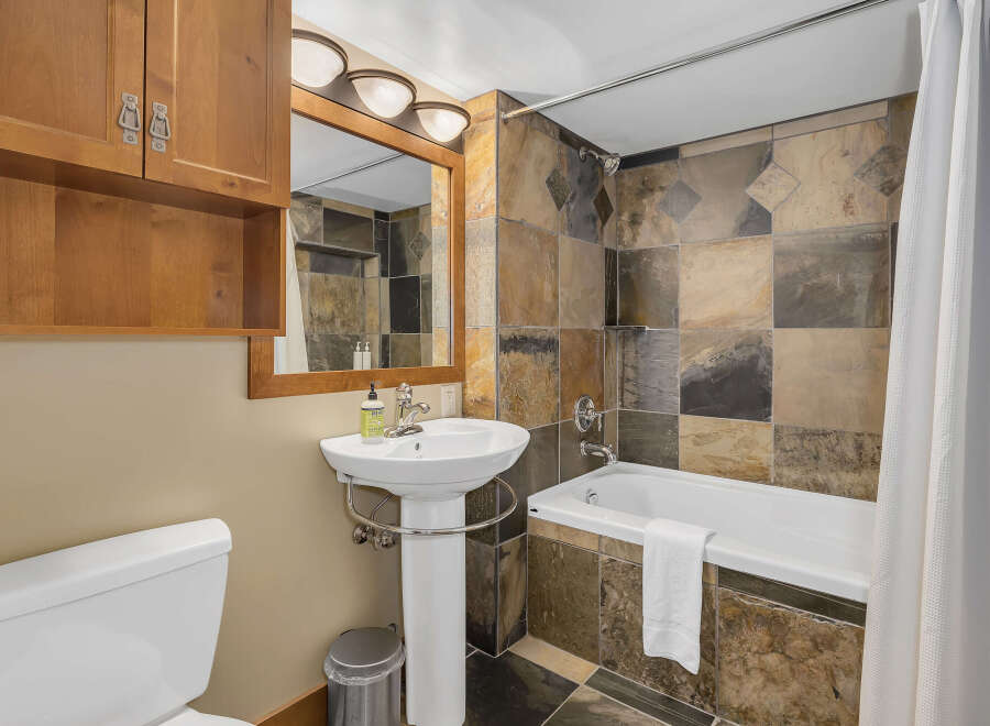 This bathroom features a stylish combination of natural stone tiles and warm wood cabinetry.