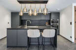 Experience modern luxury in this sleek, dark gray kitchen featuring a spacious island with a built-in sink and elegant pendant lighting.