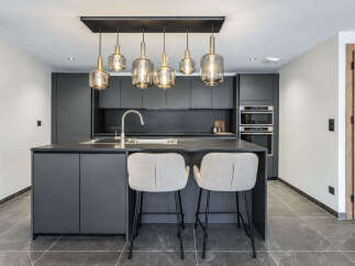 Experience modern luxury in this sleek, dark gray kitchen featuring a spacious island with a built-in sink and elegant pendant lighting.