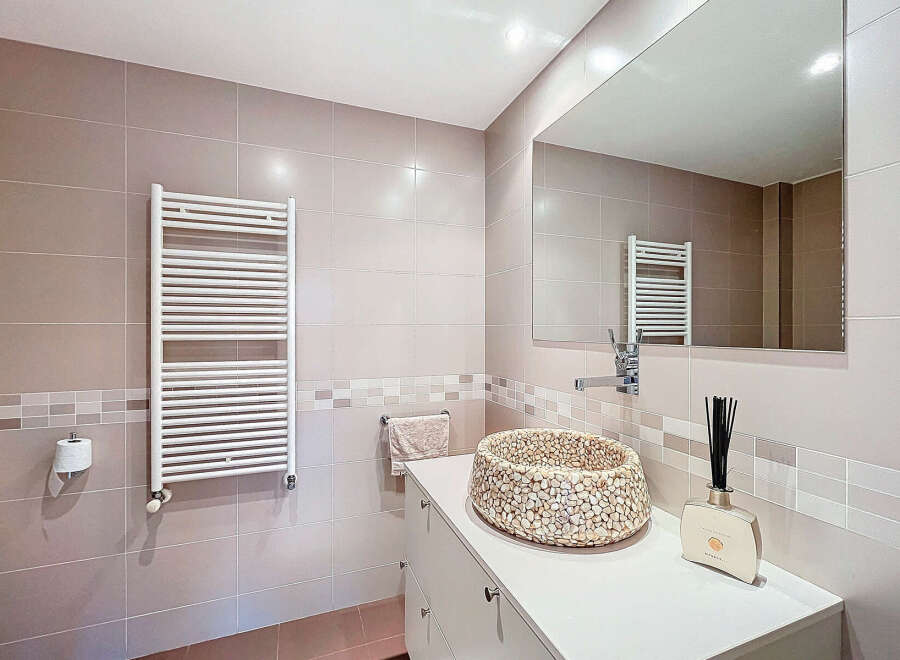 This modern bathroom features a stylish pebble-stone sink, a sleek white towel warmer, and a large mirror.