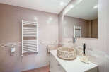 This modern bathroom features a stylish pebble-stone sink, a sleek white towel warmer, and a large mirror.