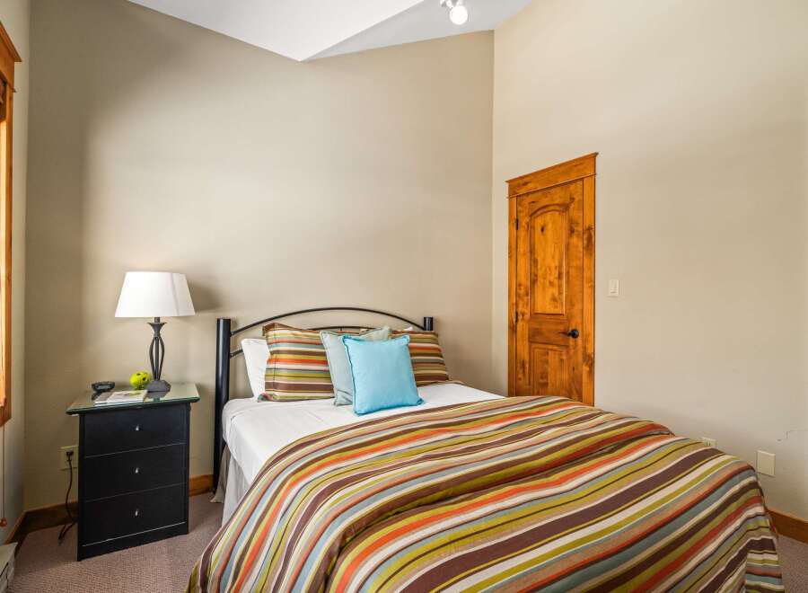 This cozy bedroom features a comfortable bed with a colorful striped comforter and accent pillows, creating a warm and inviting atmosphere.