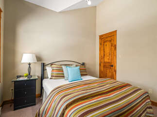 This cozy bedroom features a comfortable bed with a colorful striped comforter and accent pillows, creating a warm and inviting atmosphere.