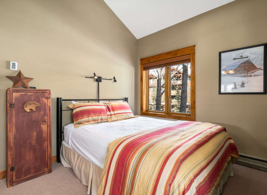 This cozy bedroom features a comfortable bed with a colorful striped comforter and pillows, creating a warm and inviting atmosphere.