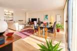 Experience modern living in this spacious open-plan apartment, featuring a bright living area with plush sofas and a stylish dining space with a glass-top table.