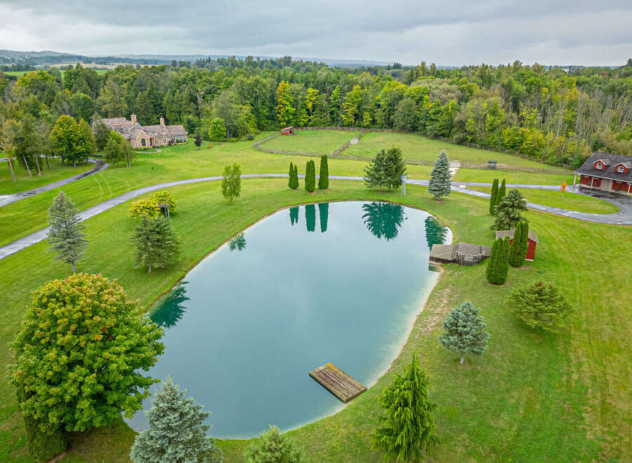 Discover a stunning estate featuring a serene pond, lush greenery, and a charming red barn.