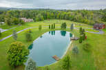 Discover a stunning estate featuring a serene pond, lush greenery, and a charming red barn.
