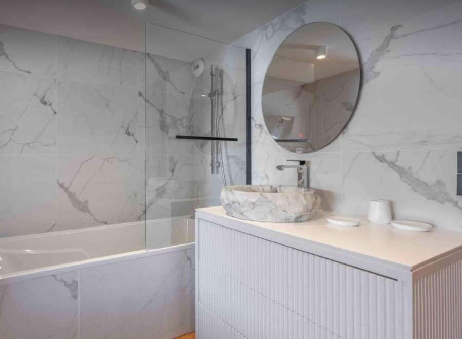 This stunning bathroom features a modern design with marble-like tiles and a sleek, white vanity.
