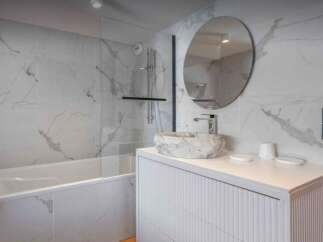 This stunning bathroom features a modern design with marble-like tiles and a sleek, white vanity.