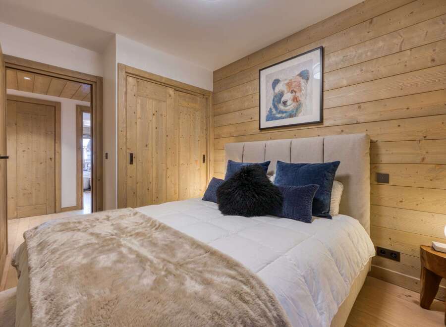 This cozy bedroom features a rustic wood-paneled wall and a comfortable bed with plush pillows.