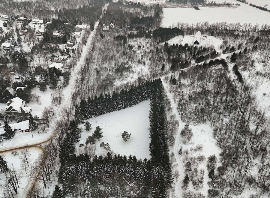 This aerial view showcases a stunning winter landscape, highlighting a unique property surrounded by a lush evergreen forest.