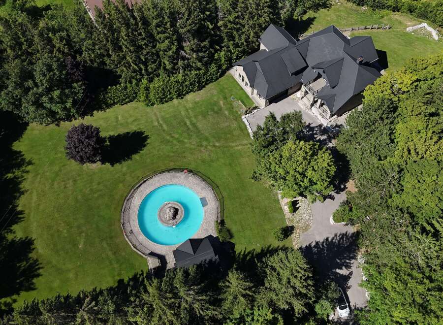 Discover this stunning property featuring a large, circular swimming pool with a central fountain, surrounded by lush green lawns and mature trees.