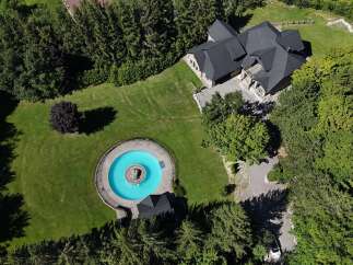 Discover this stunning property featuring a large, circular swimming pool with a central fountain, surrounded by lush green lawns and mature trees.