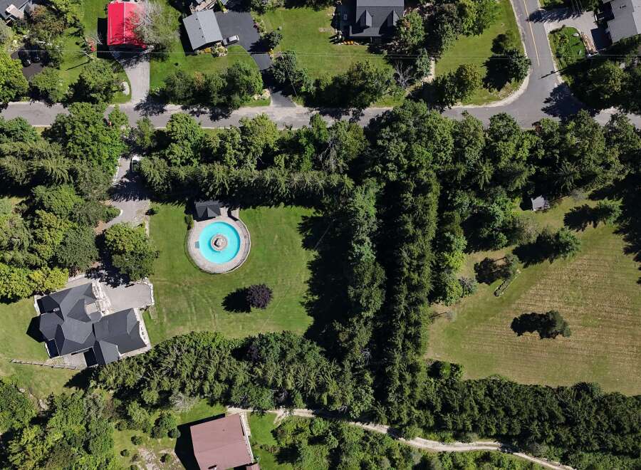 Discover this stunning aerial view showcasing a luxurious estate with a circular pool and a modern dark-roofed home.