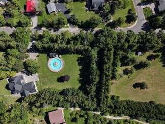 Discover this stunning aerial view showcasing a luxurious estate with a circular pool and a modern dark-roofed home.