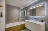 This modern bathroom features a sleek design with gray tiled walls and a wooden bathtub surround.