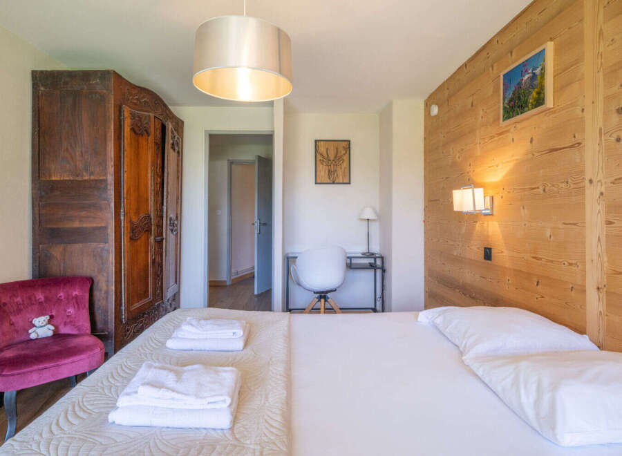 Experience cozy mountain living in this charming bedroom, featuring a plush velvet armchair and a large wooden wardrobe.
