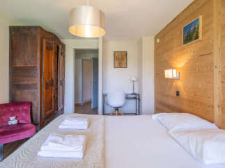 Experience cozy mountain living in this charming bedroom, featuring a plush velvet armchair and a large wooden wardrobe.