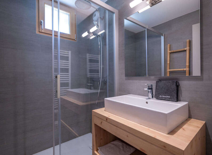 Experience modern comfort in this stylish bathroom featuring a spacious walk-in shower with sleek grey tiling and a convenient heated towel rack.