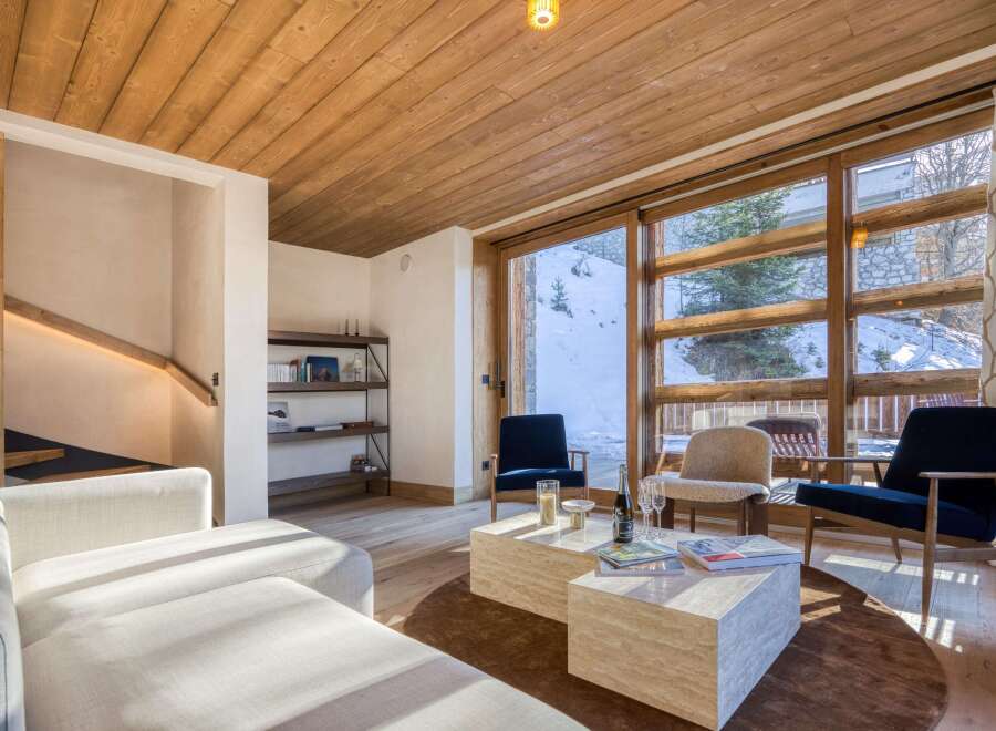 Experience luxury living in this stunning property, featuring a cozy living room with a wooden ceiling and large windows that offer breathtaking views of the snowy landscape.