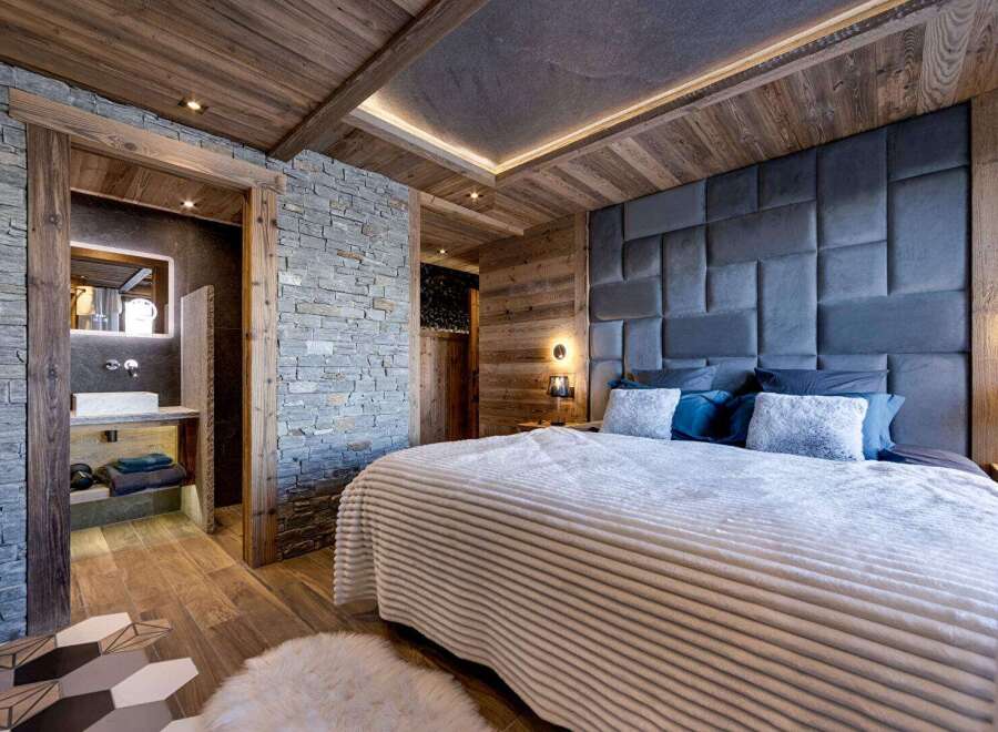 Experience luxury living in this stunning bedroom featuring a unique stone wall and wooden accents.