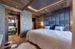 Experience luxury living in this stunning bedroom featuring a unique stone wall and wooden accents.