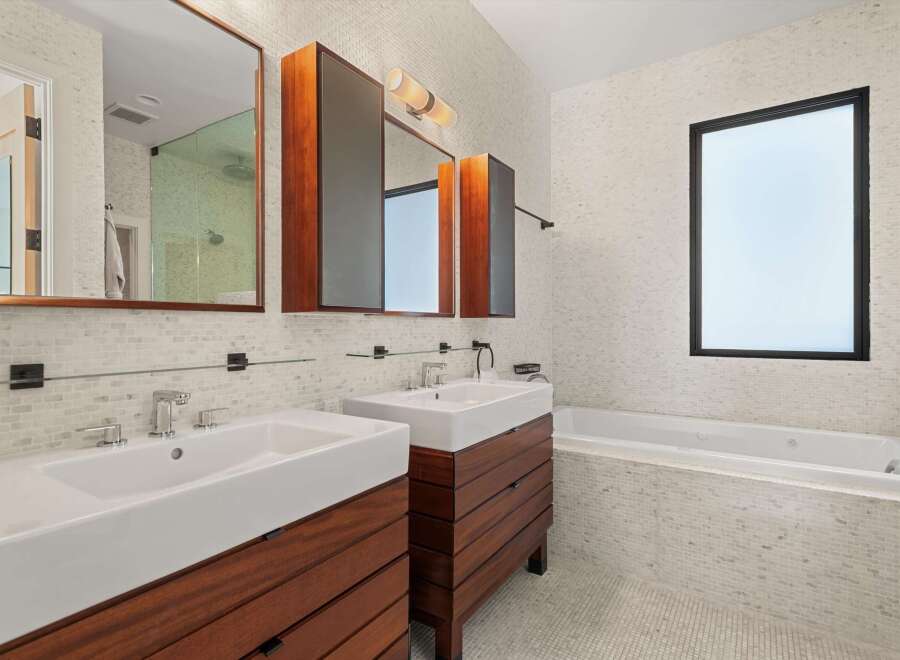 This modern bathroom boasts a sleek design with a double vanity featuring rich wood cabinetry and pristine white sinks.