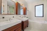 This modern bathroom boasts a sleek design with a double vanity featuring rich wood cabinetry and pristine white sinks.