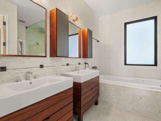 This modern bathroom boasts a sleek design with a double vanity featuring rich wood cabinetry and pristine white sinks.